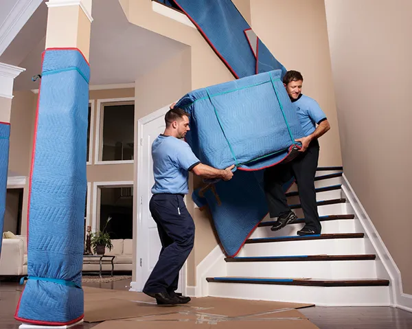 A mover uses protective wrapping to secure furniture inside a moving truck.