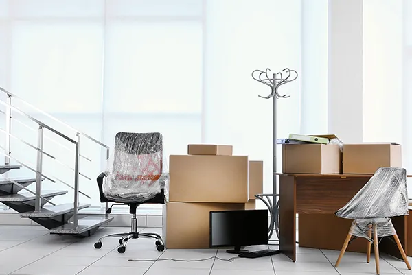 An office space shows unpacked cardboard boxes scattered around a desk and office chair, indicating a recent move and the need for unpacking services.