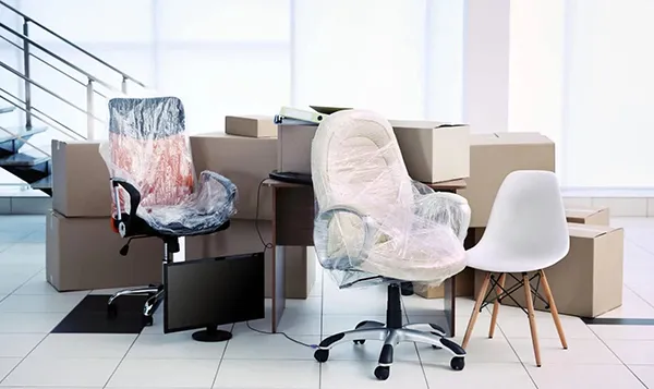A brightly lit office space shows unpacked cardboard boxes scattered around desks and chairs, suggesting a recent move.