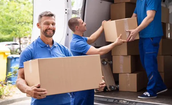 Three movers work together to unload cardboard boxes from a moving truck, handing them to each other.
