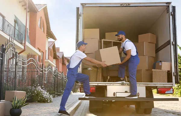 Two movers carefully lift and carry a light-colored sofa, positioning it to load into a moving truck.