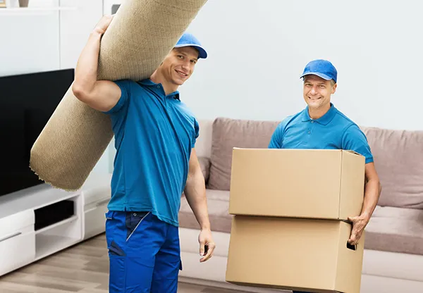 Two smiling movers carry a stacked tower of cardboard boxes.