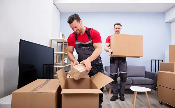 Movers unpack boxes in an office setting with desks and equipment in the background.