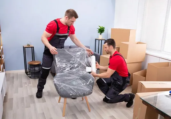 Two movers professionally wrapping furniture with protective material.