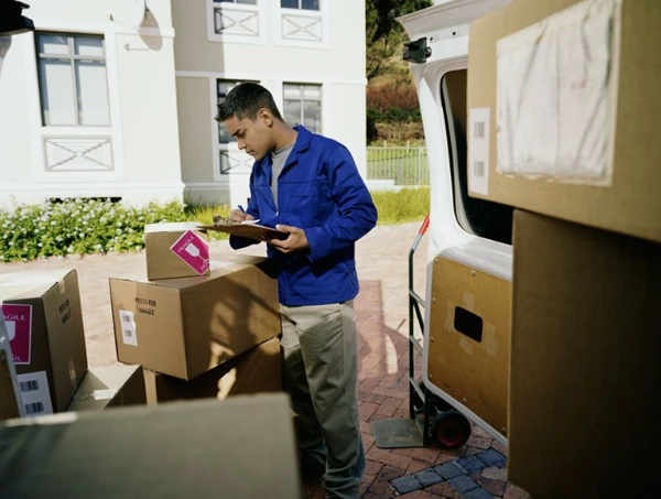 Burien WA full-service movers with a tablet organize boxes by a moving truck professionally.