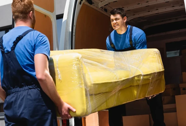 Movers carefully unloading a large, wrapped item from a truck.