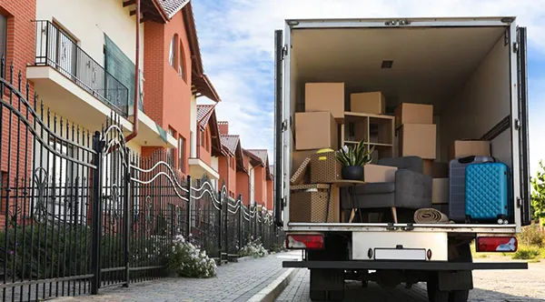 The open back of a moving truck is parked on a residential street, filled with cardboard boxes ready for unloading.