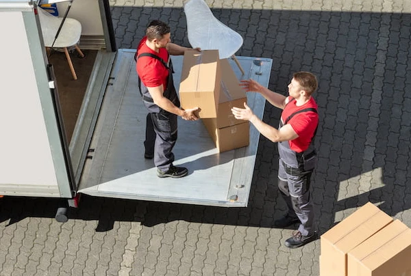 Two movers unloading boxes from a truck onto a conveyor belt.
