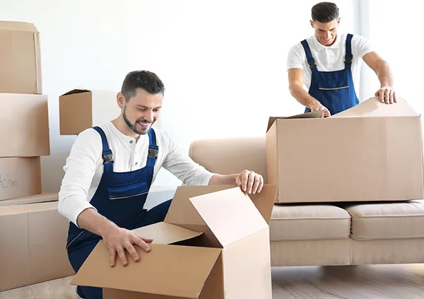 Two movers in uniform are packing items into cardboard boxes, preparing them for a move.