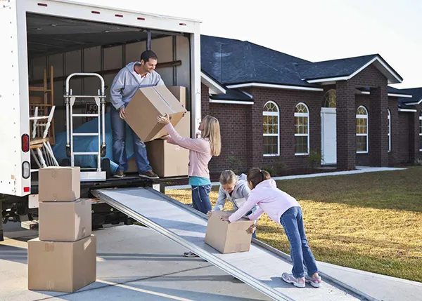 A moving truck is parked, and a person is loading or unloading cardboard boxes.