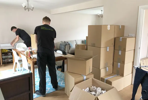 Movers packing boxes in a home, illustrating residential packing services.